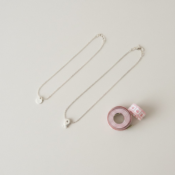 Zwei Kinderketten in unterschiedlicher Länge mit Maßband auf heller Unterlage