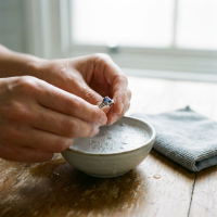 Haende reinigen einen Silberring mit Edelstein in milder Seifenlauge, daneben liegt ein weiches Mikrofasertuch